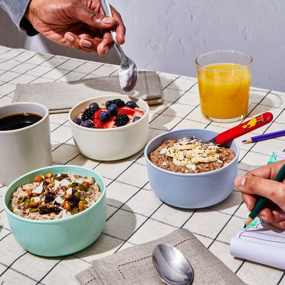 Three bowls of overnight oats with berries, banana and seeds at a breakfast table